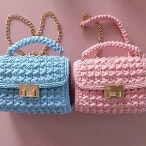 May include: Two crocheted handbags with gold chain straps. One is light blue and the other is pink.