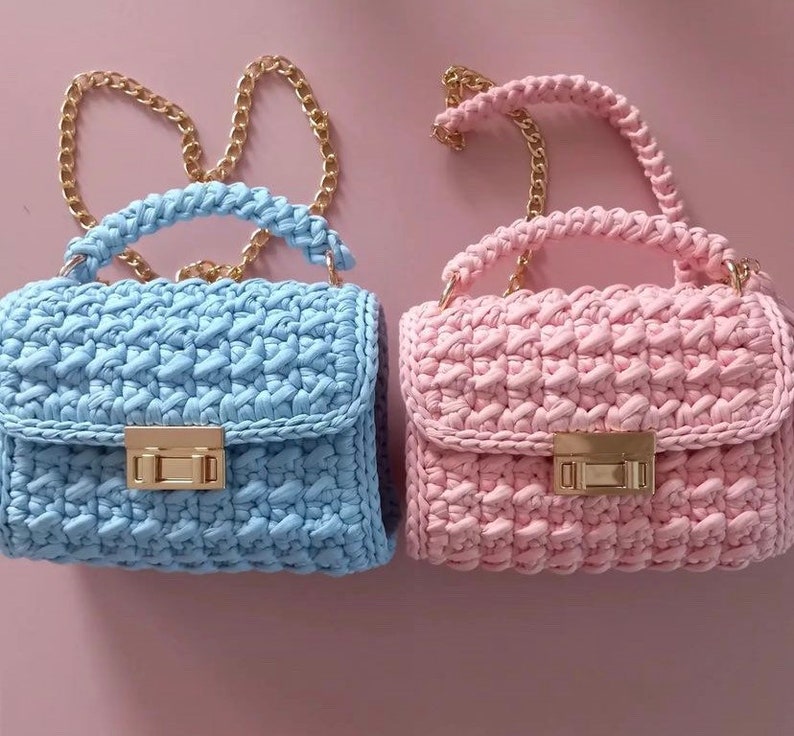 May include: Two crocheted handbags with gold chain straps. One is light blue and the other is pink.