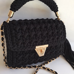 May include: A black crocheted handbag with a gold chain strap and a gold clasp. The bag has a top handle and a tassel.