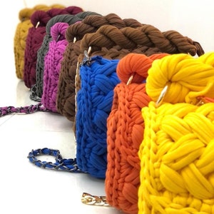 May include: A row of colourful crocheted handbags with chain straps. The bags are in shades of mustard yellow, burgundy, grey, pink, blue, orange, and yellow.