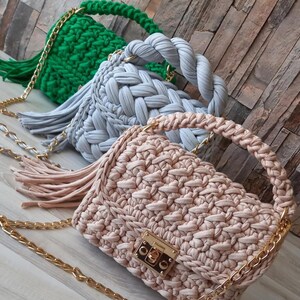 May include: Three crocheted handbags with gold chains. The handbags are in green, light blue, and beige. The beige handbag has a gold lock.