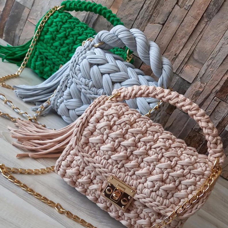 May include: Three crocheted handbags with gold chains. The handbags are in green, light blue, and beige. The beige handbag has a gold lock.