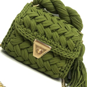 May include: A green crocheted handbag with a gold chain strap and a gold clasp. The bag has a braided handle and a tassel.