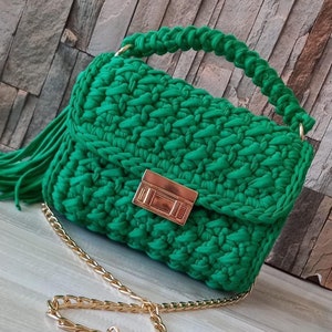May include: A green crocheted handbag with a gold chain strap and a gold clasp. The bag has a fringe detail.