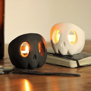 Two cute styled skulls in black and white with a matte finish. The top of the head and eyes are hollow for candlelight.