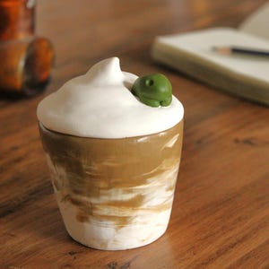 May include: A ceramic jar with a white lid and a green turtle figurine on top. The jar has a brown and white marbled design.