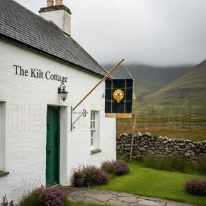 May include: A white cottage with a slate roof and a green door. The sign reads "The Kilt Cottage". A flag with a yellow emblem hangs from a wooden pole. The cottage is set in a green garden with a stone path and purple heather.