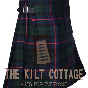 May include: A green, blue, and red tartan kilt with a leather strap and buckle closure. The kilt is made of a woven fabric and has a fringed edge. The text "THE KILT COTTAGE KILTS FOR EVERYONE" is printed on the bottom of the kilt.