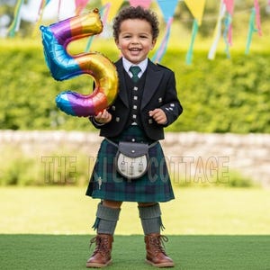 Puede incluir: Un niño con un traje tradicional escocés, sosteniendo un globo con el número 5 en colores del arcoíris. El atuendo incluye una chaqueta negra, un kilt a cuadros verdes y azules y un sporran. El fondo presenta decoraciones de fiesta y vegetación.