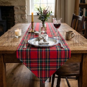 May include: A wooden dining table set for a meal, featuring a red plaid table runner. The table is set with a plate, silverware, a wine glass, and a mug. A candle and a vase of flowers add to the ambiance.