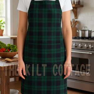 May include: Green and black plaid apron with two front pockets. The apron is worn by a person in a kitchen setting. The text "THE KILT COTTAGE" is printed on the apron. The apron is made of a durable fabric.