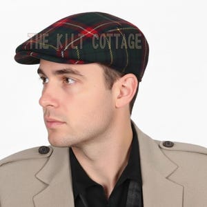 May include: A green, red, and yellow plaid flat cap with the text "THE KILT COTTAGE" on the front. The cap is worn by a person wearing a tan jacket and black shirt.