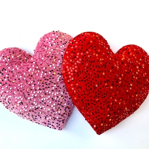 May include: Two heart-shaped pillows covered in sequins. One pillow is pink and the other is red.
