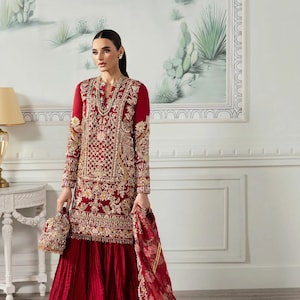 May include: A red embroidered formal dress with gold accents. The long-sleeved top features intricate gold embroidery, paired with a matching skirt and a floral-patterned shawl. A small, matching purse completes the ensemble.