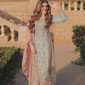 Könnte beinhalten: Ein hellblau bestickter Salwar Kameez mit passendem Dupatta. Das traditionelle südasiatische Outfit weist aufwendige Stickereien und Verzierungen in Rosa- und Silbertönen auf. Das Ensemble wird mit einer passenden Hose getragen.