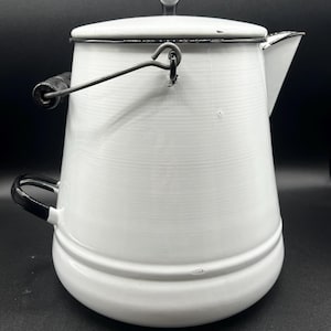 May include: White enamelware coffee pot with a black handle and spout. The pot has a lid with a small knob and a wire handle. The pot is a classic design, perfect for camping or home use.