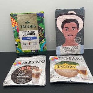 Könnte beinhalten: Zwei rechteckige Reißverschlusstaschen aus recycelten Kaffeeverpackungen. Eine zeigt ein buntes tropisches Muster mit Jacobs Origins Branding, die andere eine stilisierte Illustration einer Person mit Hut und Espresso-Aufschrift.