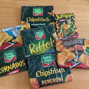 Könnte beinhalten: Eine Auswahl an Chipstüten der Marken "Funny-Frisch" und "Jumpys". Die Tüten sind hauptsächlich dunkelgrün mit farbenfrohen Grafiken und Texten, die die Marke und die Geschmacksrichtungen hervorheben. Es sind verschiedene Snack-Produkte zu sehen.