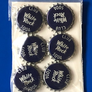 Puede incluir: Seis tapones de botella de soda White Rock vintage en una bolsa de plástico transparente. Los tapones son plateados con centros azules y letras blancas que dicen "White Rock Soda Club".