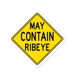 Puede incluir: Una pegatina amarilla en forma de diamante con un borde negro. La pegatina presenta el texto "MAY CONTAIN RIBEYE" en letras mayúsculas negras y en negrita. La pegatina está diseñada para parecerse a una señal de tráfico.