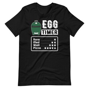 May include: Black t-shirt featuring a green and white illustration of a barbecue grill with the text "Egg Timer". The illustration includes a chart with the text "Rare", "Med", "Well", and "Pizza" and a visual representation of the cooking time using beer mugs.