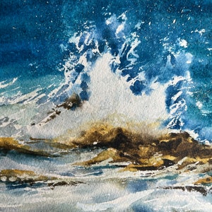 May include: A watercolour painting depicting a crashing wave against a rocky shore. The wave is white with blue and grey tones, and the rocks are brown with hints of gold. The background is a deep blue with white speckles.