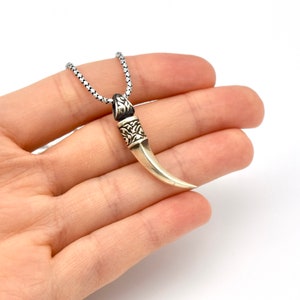 May include: Silver chain necklace with a silver pendant shaped like a fang with intricate details.