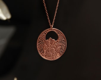 May include: A rose gold necklace with a circular pendant featuring a delicate floral design.