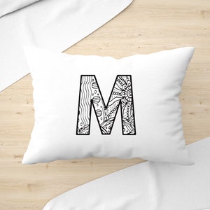 May include: A white pillow with a black and white patterned letter M in the centre.