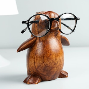 May include: A wooden penguin figurine with black round glasses. The penguin is brown and has a smooth, polished finish.