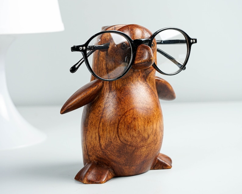May include: A wooden penguin figurine with black round glasses. The penguin is brown and has a smooth, polished finish.