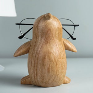 May include: A wooden penguin figurine with glasses perched on its beak. The penguin is brown and has a smooth, polished finish.