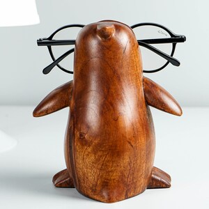 May include: A wooden penguin figurine with glasses perched on its beak. The penguin is brown and has a smooth, polished finish.