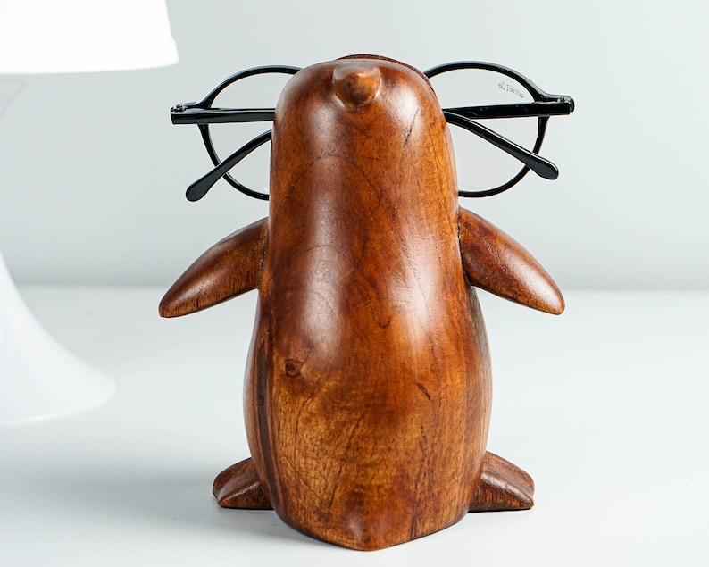 May include: A wooden penguin figurine with glasses perched on its beak. The penguin is brown and has a smooth, polished finish.