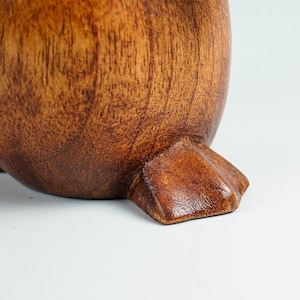 May include: Close-up of a wooden penguin figurine's foot. The foot is carved with detail and has a dark brown stain.