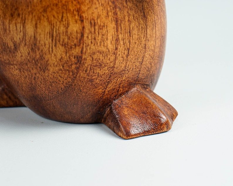 May include: Close-up of a wooden penguin figurine's foot. The foot is carved with detail and has a dark brown stain.