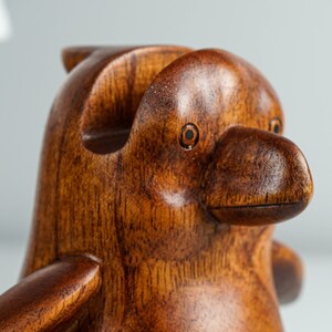 May include: A wooden penguin figurine with a brown finish. The penguin has a detailed beak and eyes.