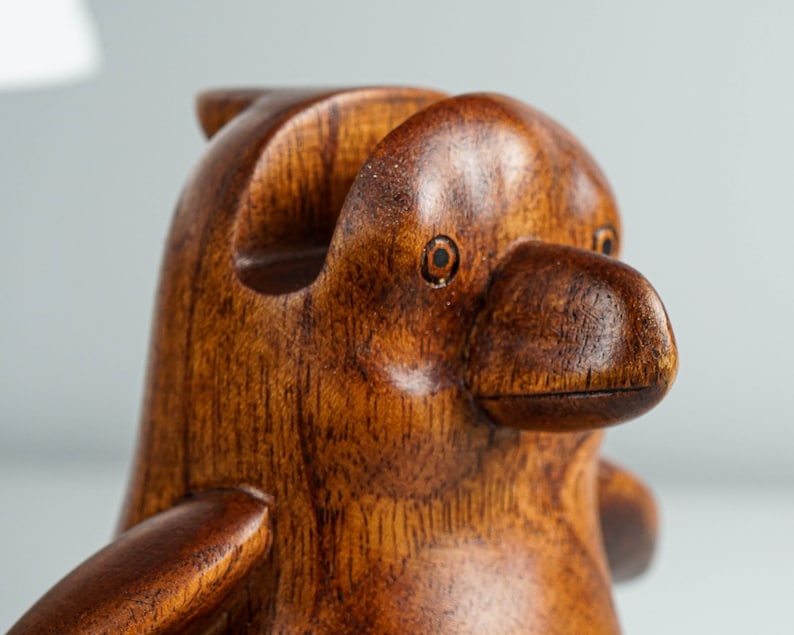May include: A wooden penguin figurine with a brown finish. The penguin has a detailed beak and eyes.