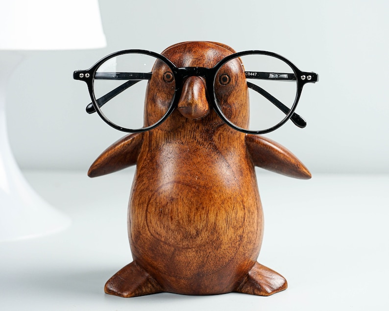May include: A wooden penguin figurine with black round glasses perched on its beak. The penguin is brown and has a smooth, polished finish.