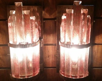 Könnte beinhalten: Zwei Wandleuchten mit mattierten Glasschirmen. Die Schirme bestehen aus vertikalen Glasstäben und haben eine warme, bernsteinfarbene Tönung. Die Leuchten sind an einer Holzwand montiert.