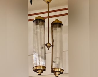 May include: A brass and glass chandelier with two cylindrical shades. The shades are made of clear glass with vertical lines.
