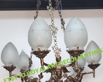 May include: A 6-light antique brass chandelier with frosted glass shades. The chandelier features a central design of a woman holding a fish, with decorative scrolls and floral accents. The shades have a star pattern etched into the glass.