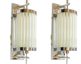 May include: Pair of chrome wall lights with frosted glass shades. Each light has a cylindrical shade with vertical lines and a chrome arm extending from the wall mount.
