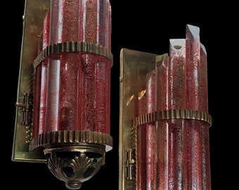 Könnte beinhalten: Paar Vintage-Wandleuchten mit roten Glasschirmen und messingfarbenen Metallakzenten. Die Schirme haben ein strukturiertes Muster und sind zylindrisch mit einem abgestuften Oberteil. Die Leuchten haben eine rechteckige Rückplatte und einen dekorativen Sockel.