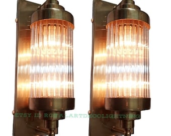May include: Two brass wall sconces with clear glass shades. Each shade is made of vertical glass rods. The sconces are mounted on a brass plate.