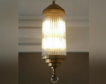 May include: A brass and glass pendant light with a cylindrical shade featuring vertical glass panels. The light has a clear glass orb at the bottom.