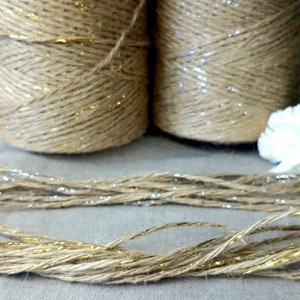 May include: Two spools of natural jute twine with gold glitter accents. The twine is unwound and lying on a light beige surface.