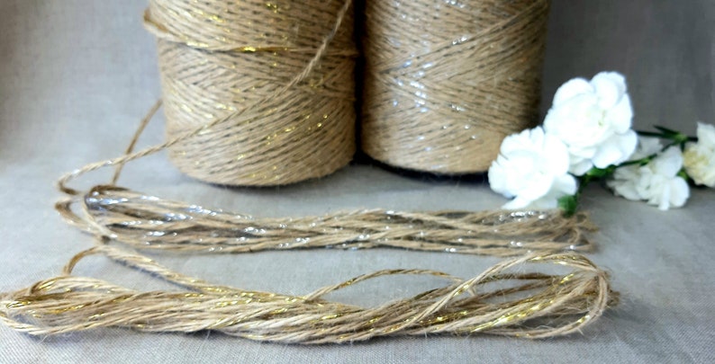 May include: Two spools of natural jute twine with gold glitter accents. The twine is unwound and lying on a light beige surface.