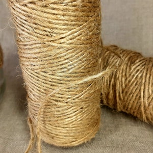 May include: A close-up of two spools of natural brown twine. The twine is wound tightly around the spools and is ready to be used for crafting or other projects.
