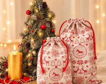 May include: Two beige drawstring gift bags featuring a red Nordic-style pattern of rocking horses, snowflakes, and trees. The bags are made of a woven fabric and have bright red cord closures. They are positioned next to a gold candle and tree.